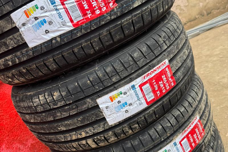 Stack of new Fronway 265/55 ZR19 tyres with EU labels outside a tyre shop