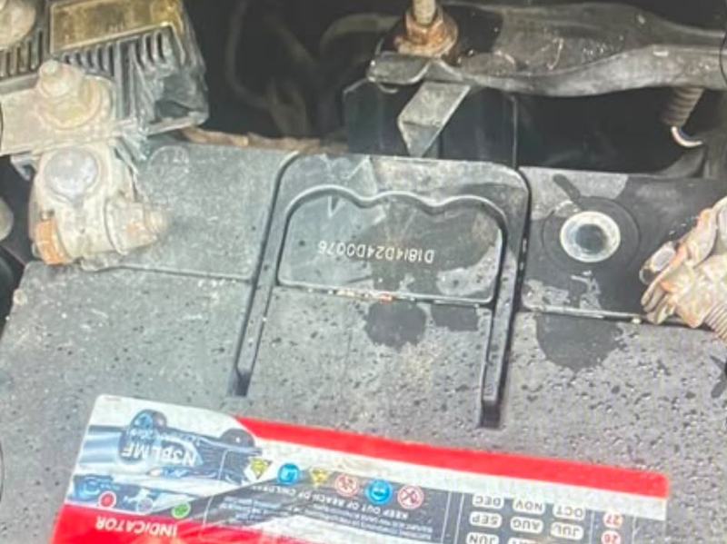 Car battery in an engine bay with white and brown crust corroding the terminals