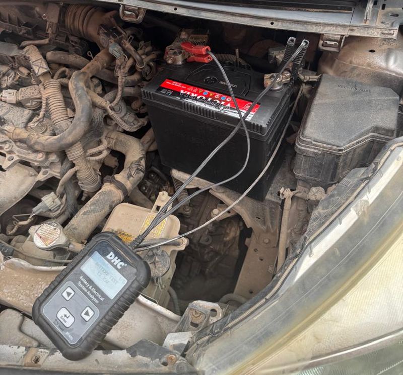 Battery and electrical system analyzer connected to a car battery in an engine bay